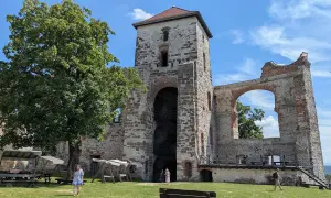 Ruiny zamku Tenczynek z wieżą i łukiem, na tle błękitnego nieba z chmurami.