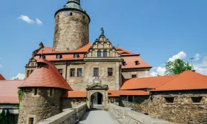Zamek Czocha, malownicza trasa turystyczna. Kamienne mury, czerwone dachy i wieża zamkowa pod błękitnym niebem.