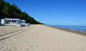 Plaża w Pobierowie z białymi budynkami i niebieskimi markizami, idealne miejsce na wakacyjne atrakcje nad morzem.