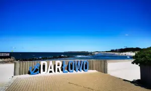 Napis "DARŁOWO" na plaży, zapraszający do odkrywania atrakcji nad Bałtykiem.