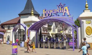 Wejście do Legendii, jednego z parków rozrywki w Polsce. Rodziny wchodzą przez bramki pod fioletowym łukiem z napisem "LegendiA".