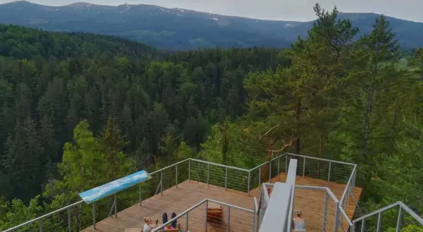 Drewniany punkt widokowy w Karpaczu z widokiem na góry i las. Dwie osoby odpoczywają na platformie.