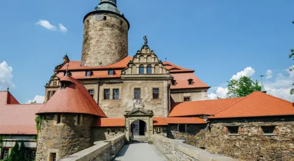 Zamek Czocha, malownicza trasa turystyczna. Kamienne mury, czerwone dachy i wieża zamkowa pod błękitnym niebem.