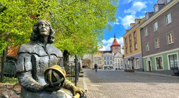 Pomnik Kopernika, jedna z głównych atrakcji Olsztyna, na tle kolorowych kamienic i błękitnego nieba.