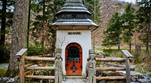 Kapliczka "Ave Maria" w Dolinie Kościeliskiej, otoczona drewnianym płotem i rzeźbami.