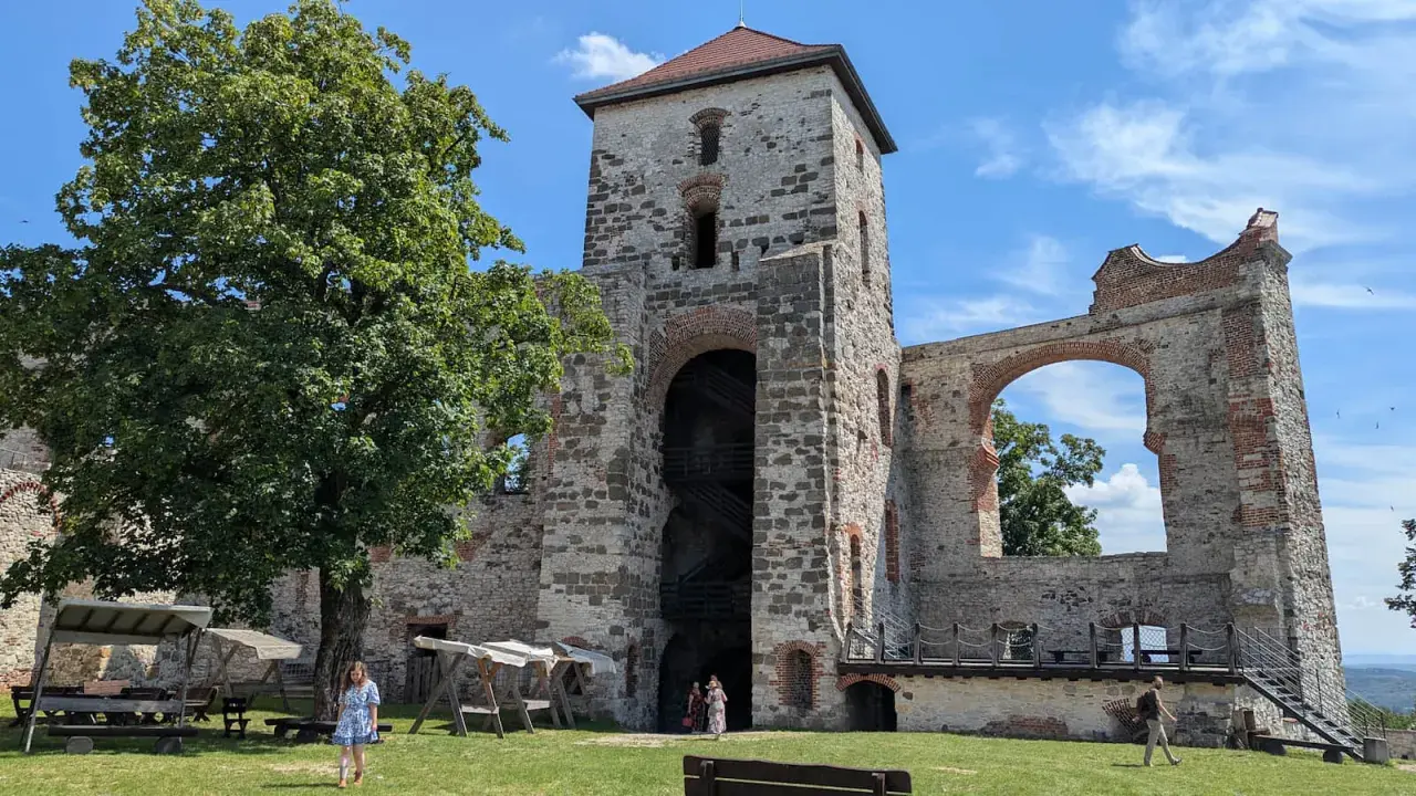 Ruiny zamku Tenczynek z wieżą i łukiem, na tle błękitnego nieba z chmurami.