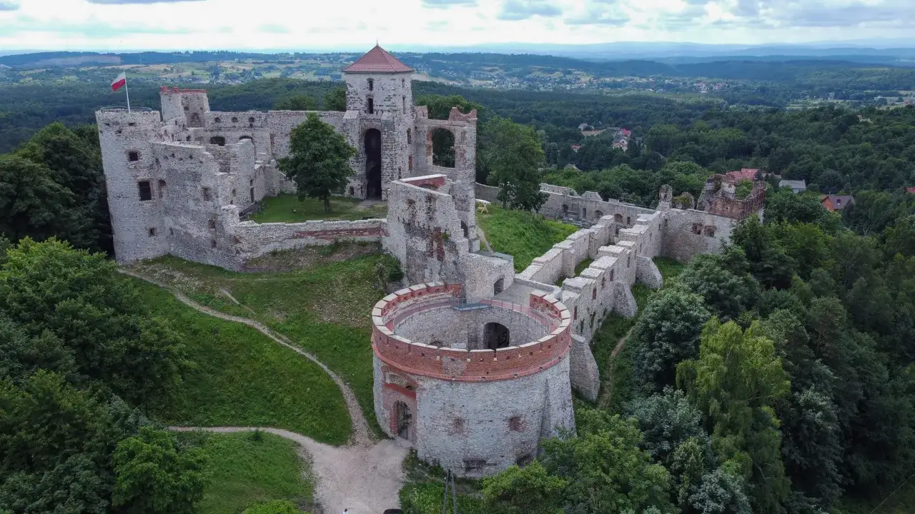 Ruiny zamku Tenczynek na wzgórzu, otoczone zielenią, z widokiem na dolinę.