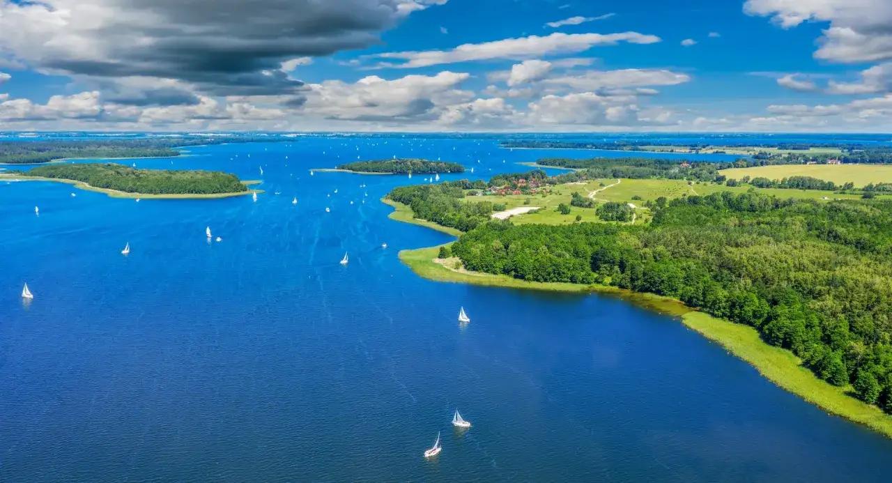 Mazury: fajne miejsce na wakacje z dzieckiem w Polsce. Jezioro pełne żaglówek, zielone wyspy i słoneczna pogoda. Idealne dla całej rodziny.