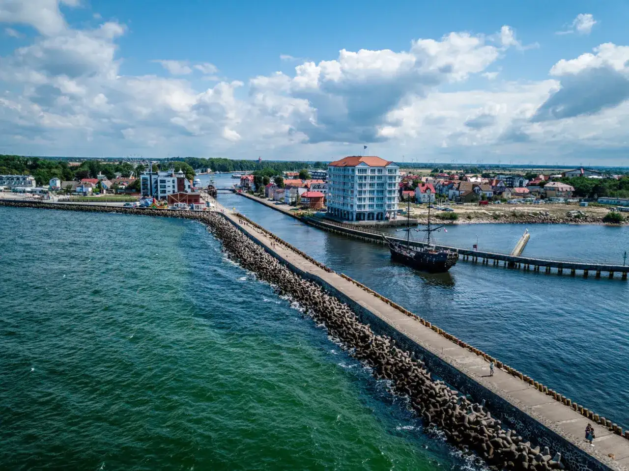 Widok na port w Darłowie z falochronem, statkiem pirackim i budynkami. To jedne z wielu darłowo atrakcje.