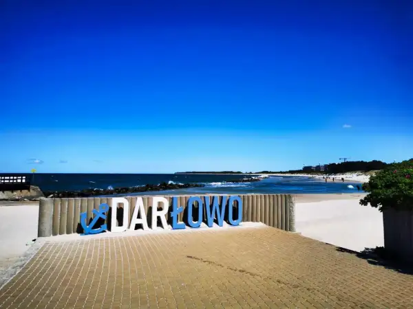 Napis "DARŁOWO" na plaży, zapraszający do odkrywania atrakcji nad Bałtykiem.