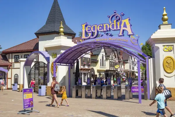 Wejście do Legendii, jednego z parków rozrywki w Polsce. Rodziny wchodzą przez bramki pod fioletowym łukiem z napisem "LegendiA".